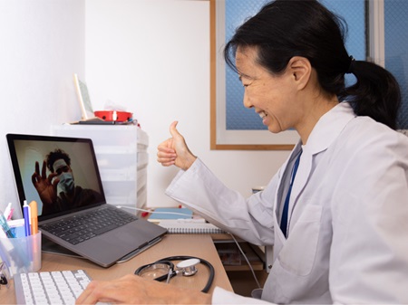 微笑提供者坐在笔记本电脑前手势的大拇指戴面具的病人在她的屏幕在一个虚拟访问