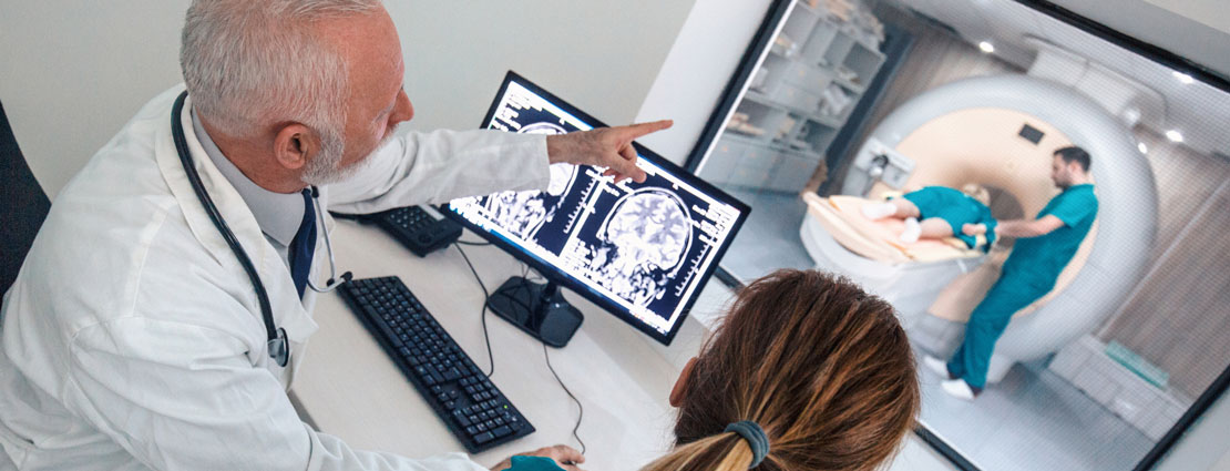 医生和护士在电脑显示器前看着病人做核磁共振